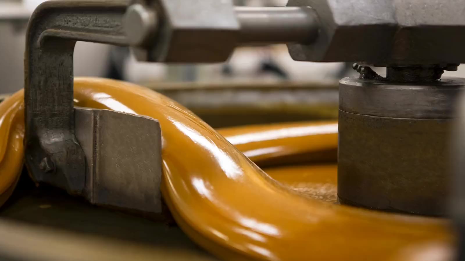 A thick ribbon of glossy golden caramel folding over itself under the steel arms of a creaming machine